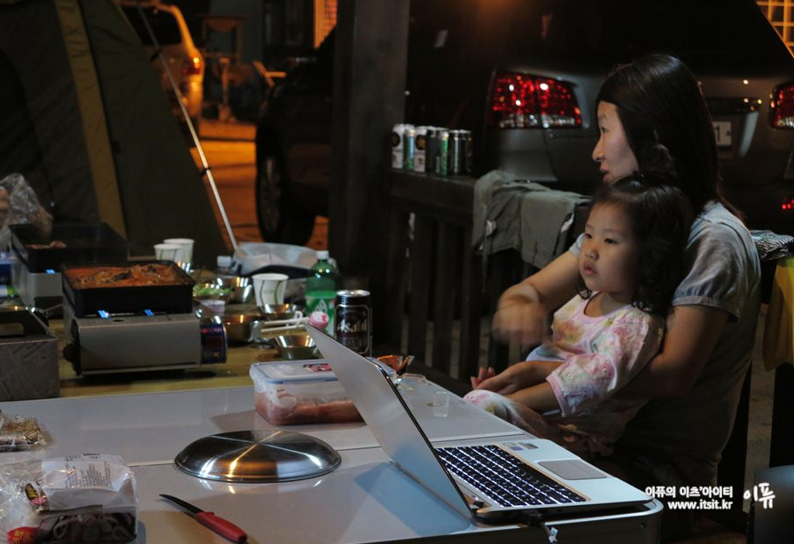 어린 여자 아이와 엄마가 캠핑장에서 LG 미니빔 TV를 시청하고 있다. 