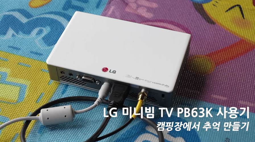 캠핑장 내 바닥에 설치된 매트 위에 LG 미니빔 TV가 놓여져 있는 모습이다. 본체 뒷편에 각종 전선이 꽂혀져 있다.