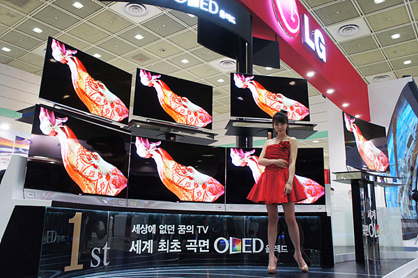 세계 최초 곡면 OLED TV가 7대 전시되어 있는 가운데 여자 모델이 포즈를 취하고 있다.