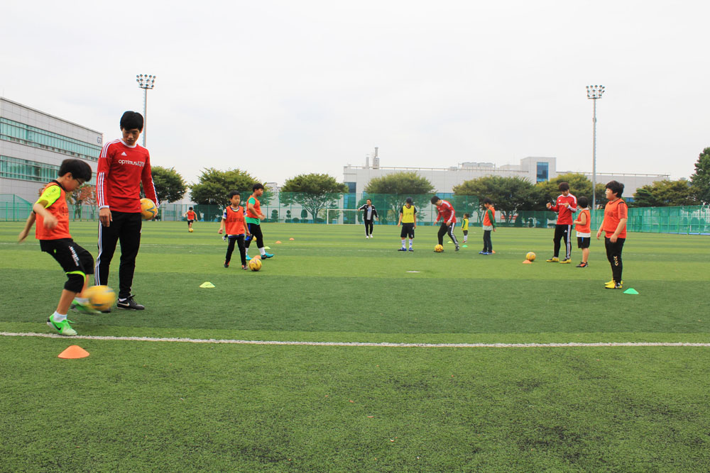 봉사단원들이 잔디축구장에서 아이들에게 축구를 가르쳐주고 있는 모습이다. 삼삼오오 짝을 이뤄 공을 가지고 연습하고 있다.