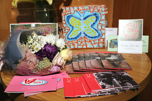 탁자 위에 나비 그림과 꽃다발, 여러 개의 책자가 올려져 있다.