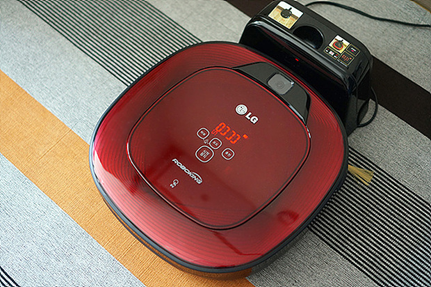 붉은 색을 띠며 네모둥글한 모습을 가진 LG 로보킹이 바닥에서 검은색 충전기를 통해 충전되고 있다.