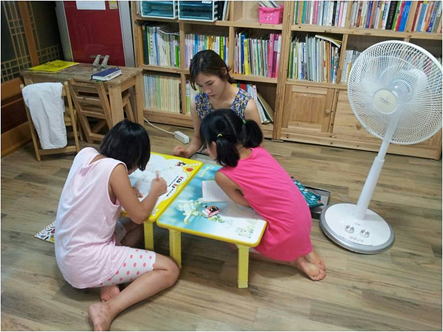 초등학교 저학년 아이들을 위해 쉽고 재미있는 영어교실을 운영하는 Sweet Home 팀. 좌식 책상 앞에 아이들 두 명과 앉아 공부하고 있는 모습 