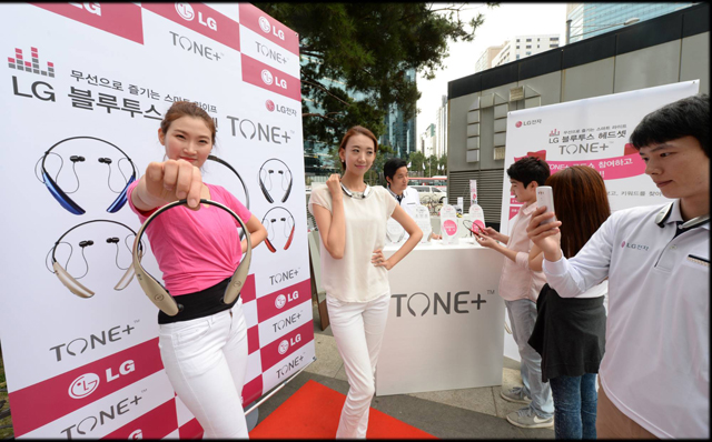 모델이 서울 강남역 행사장에서 'LG 톤플러스'를 손에 들고 포즈를 취하고 있습니다.