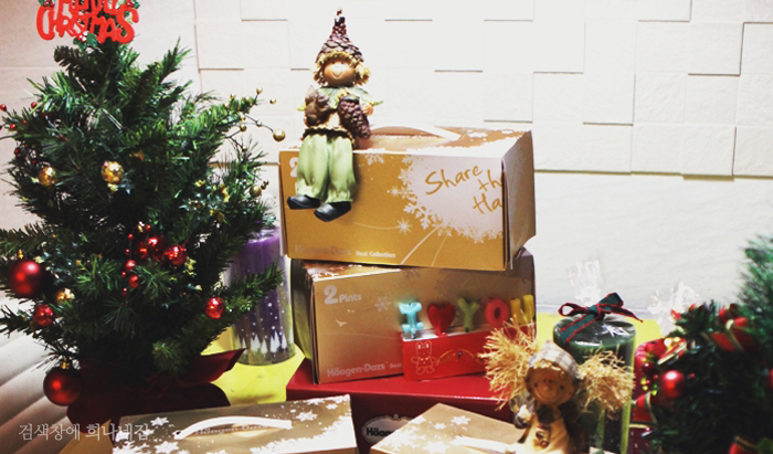 크리스마스 트리와 쌓여있는 선물 상자 위로 인형이 놓여져 있다. 