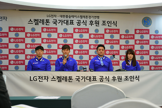 LG전자 스켈레톤 국가대표 공식 후원 조인식 현장. 네 명의 남녀 선수들이 파란색 단복을 입고 단상 테이블에 앉아있다. 