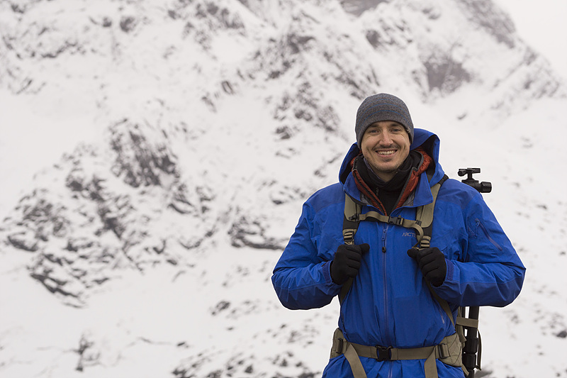 사진작가 콜비 브라운이 파란색 점퍼를 입고 눈이 덮인 산을 배경으로 서 있다. 