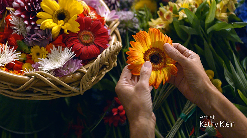 캐시 클라인이 작품의 재료가 되는 꽃을 손으로 들고 있다.