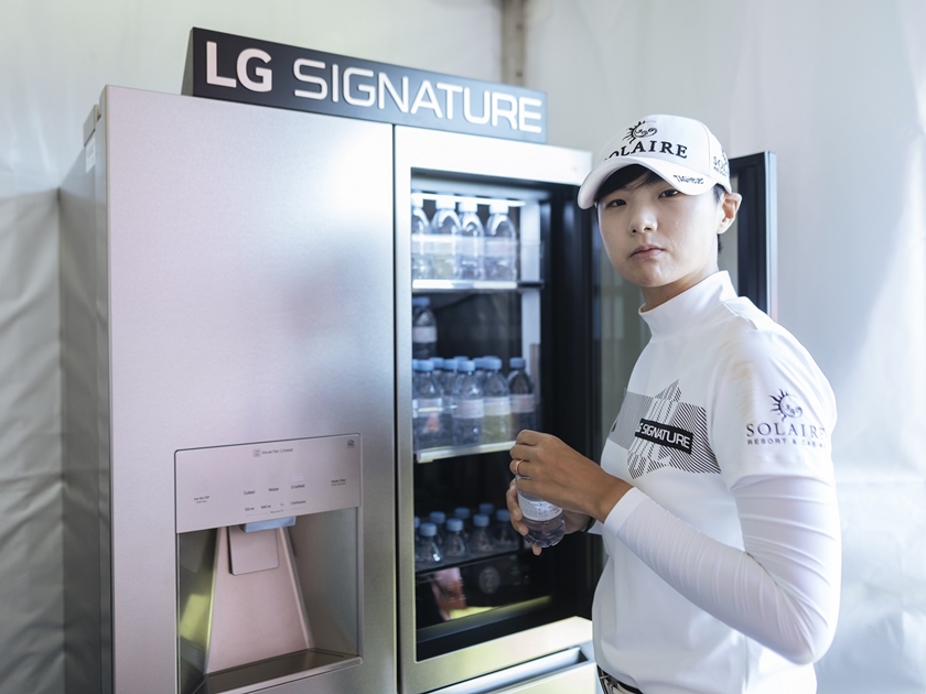 1번홀 내 LG 시그니처 체험존에서 박성현 선수가 냉장고 안의 에비앙 생수를 꺼내 마시며 직접 제품을  체험해보고 있다.
