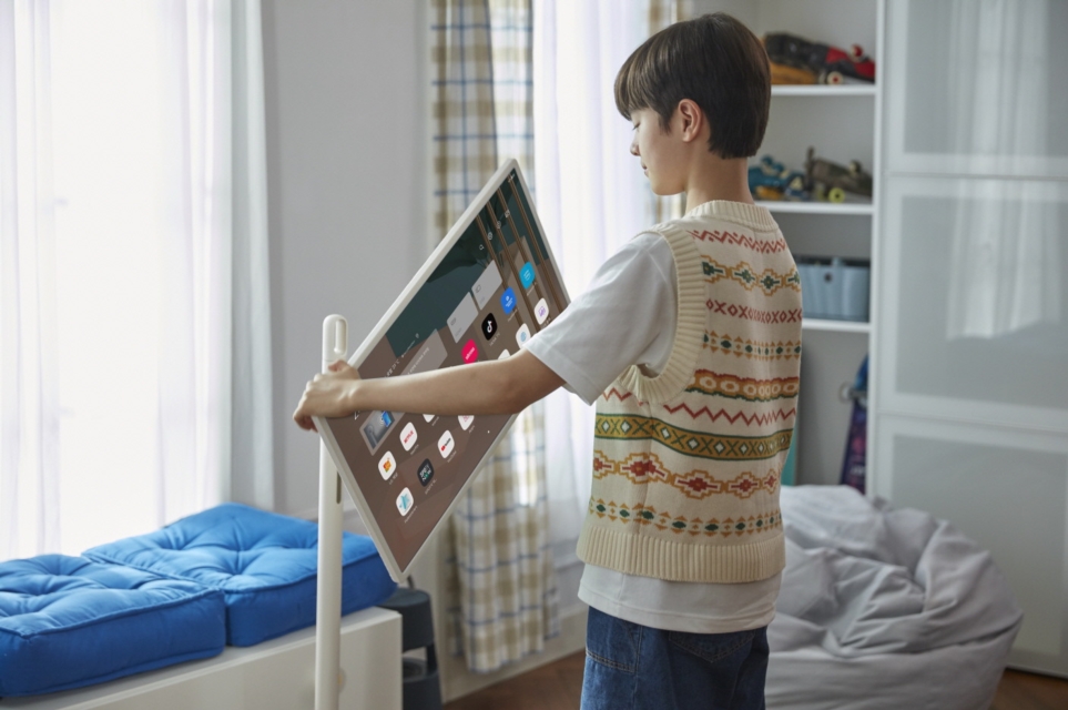 남자 아이가 방에 놓인 이동형 무선 스크린 LG 스탠바이미의 스크린 각도를 조절하고 있다.