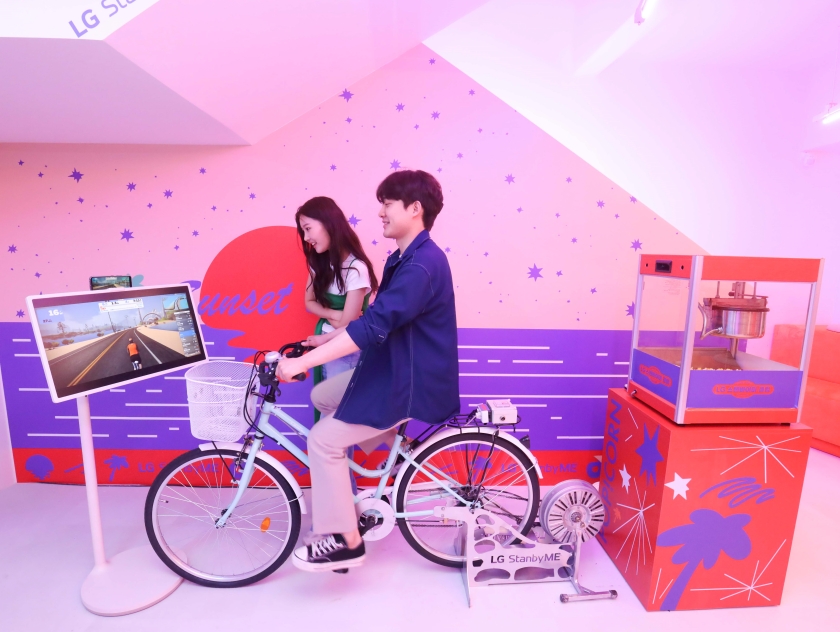  LG전자가 6월 30일부터 7월 28일까지 서울 홍대 걷고싶은거리에 LG 스탠바이미(StanbyME)를 자유롭게 경험할 수 있는 ‘LG 스탠바이미 클럽’을 오픈한다. 모델들이 LG 스탠바이미와 자전거 시뮬레이션 앱인 즈위프트(Zwift)를 연동해 실내 자전거로 사이클을 체험하고 있다.