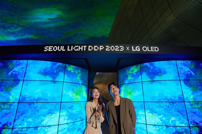 서울 라이트 DDP 2023에서 LG전자가 선보인 LG 올레드 화면에 오로라가 송출되고 있다. 그 앞에서 주변을 감상중인 두 남녀 모델의 모습