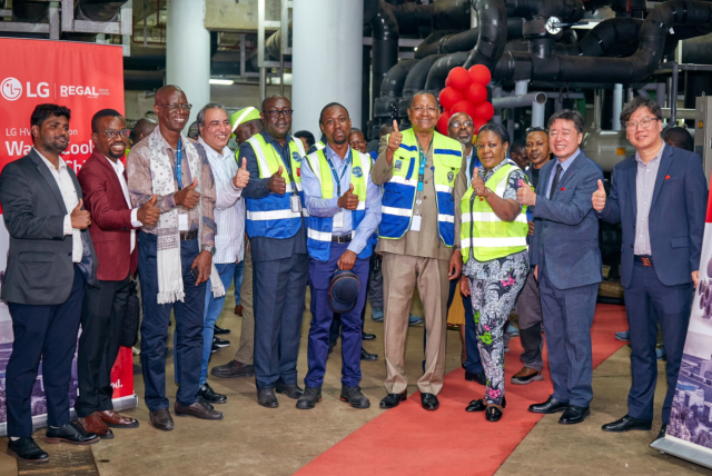 여러 명의 사람들이 LG와 REGAL 로고가 보이는 현장에서 모여 서 있다. 가운데는 안전 조끼를 입은 사람들이 있으며, 모두 엄지손가락을 들어 올리며 카메라를 향해 웃고 있다.