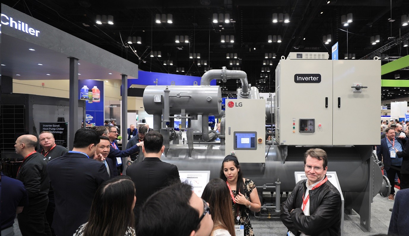 전시회 현장에서 LG 로고가 붙은 대형 인버터 칠러 장비가 설치되어 있고, 많은 사람들이 장비 주변에 모여 설명을 듣거나 이야기를 나누고 있다.