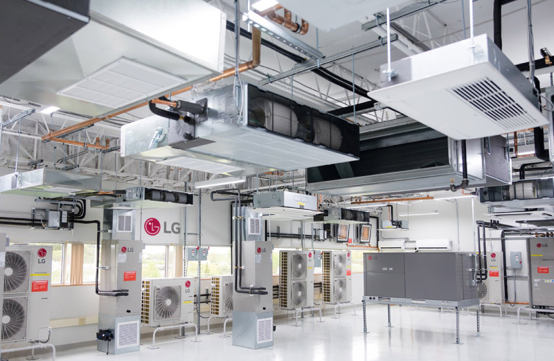 실내 HVAC(냉난방 공조) 테스트 공간으로, 천장과 벽에 여러 대의 LG 에어컨 실내기와 실외기, 덕트와 배관이 설치되어 있다. 흰색 바닥과 밝은 조명 아래 깔끔하게 정리된 시설 모습이 보인다.