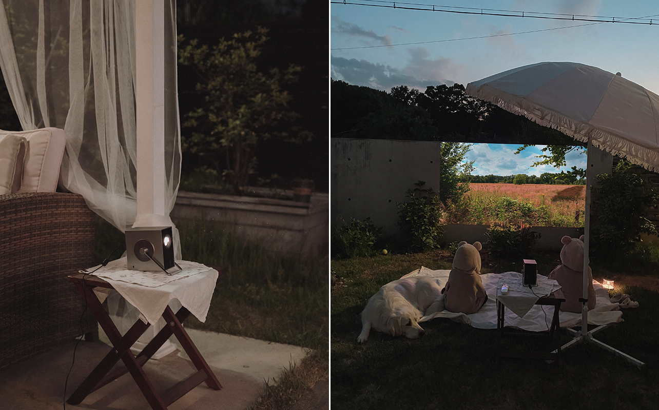 왼쪽 장면에서는 어두운 야외 공간에서 작은 접이식 테이블 위에 시네빔 큐브가 놓여 있고, 커튼처럼 드리워진 하얀 천과 라탄 소파가 아늑한 분위기를 만든다. 오른쪽 장면에서는 잔디 위에 돗자리를 펴고 시네빔 큐브가 들판 풍경을 벽에 투사하고 있으며, 두 명의 아이가 동물 후드를 쓰고 앉아 있고 옆에는 큰 개가 누워 있다. 파라솔과 작은 조명 덕분에 캠핑 같은 따뜻한 무드가 연출된 야외 홈시네마 장면이다.