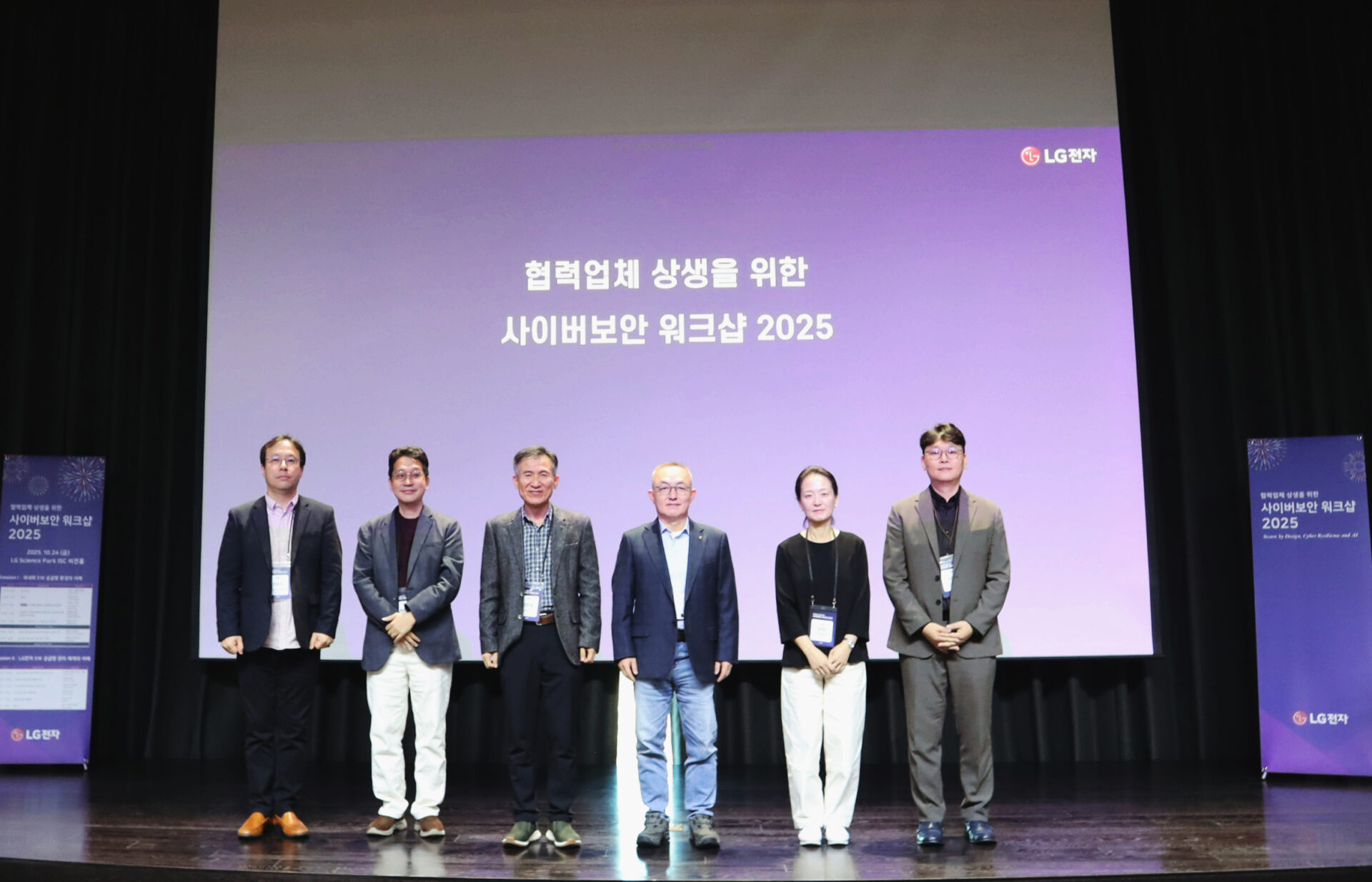 무대 위에서 여섯 명의 인물이 나란히 서서 단체 사진을 찍고 있다. 배경 스크린에는 ‘협력업체 상생을 위한 사이버보안 워크샵 2025’라는 문구와 LG전자 로고가 표시되어 있다. 양쪽에는 행사 배너가 세워져 있다.