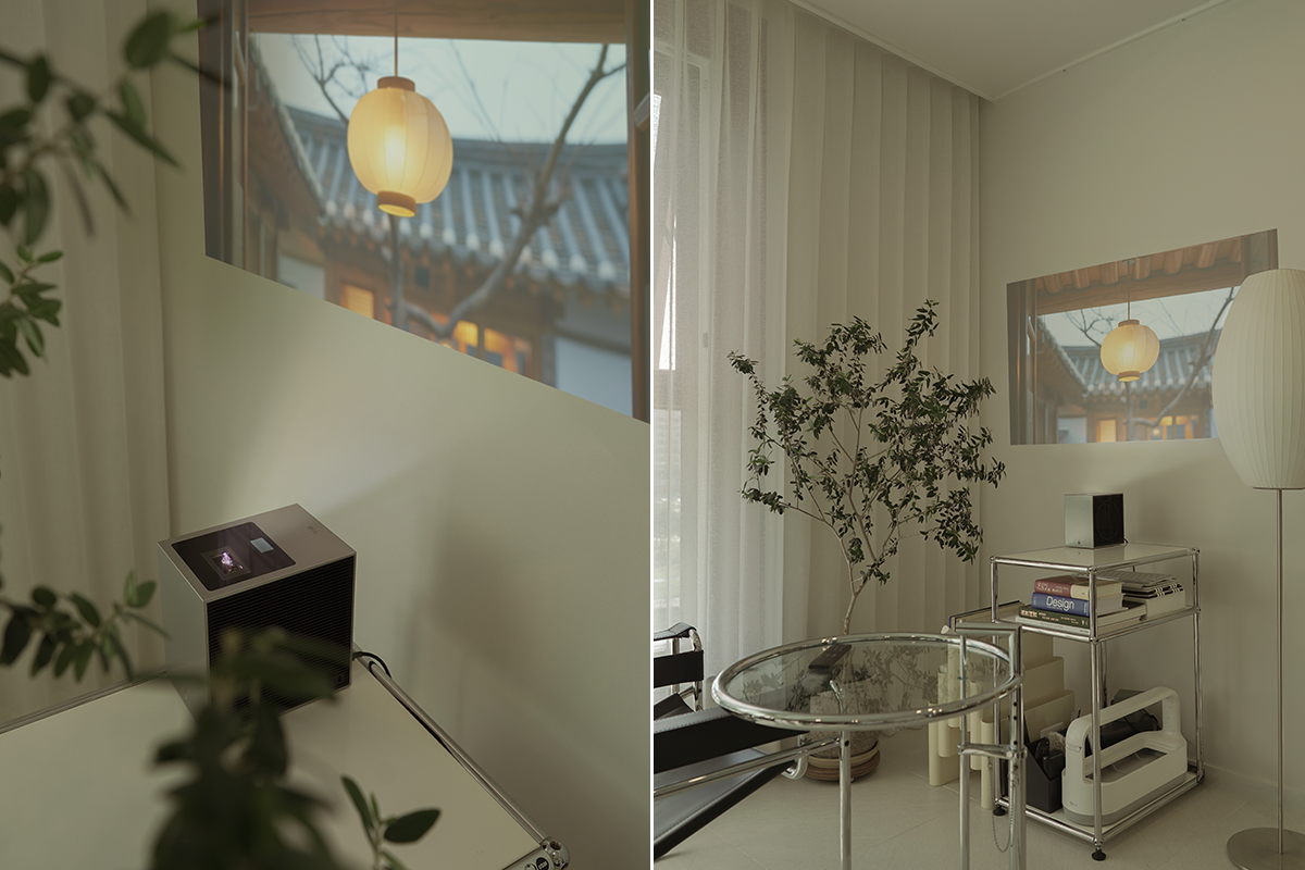 왼쪽 장면에서는 벽에 한옥 풍경이 투사되고, 테이블 위에 상단 투사창이 보이는 시네빔 쇼츠가 놓여 있으며 식물 잎이 화면 일부를 가리고 있다. 오른쪽 장면에서는 금속 선반 위의 시네빔 쇼츠가 같은 한옥 장면을 벽에 비추고 있고, 옆에는 큰 화분과 긴 스탠드 조명이 배치되어 있다. 선반 아래에는 ‘Design’이라는 책이 보이고 유리 테이블과 의자가 있는 미니멀한 거실이 연출되어 있다.