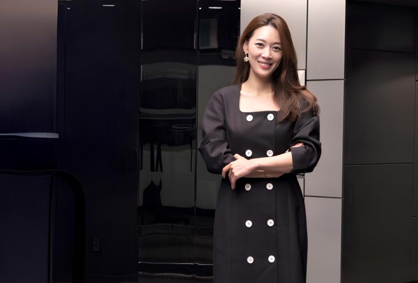 어두운 색 유광 패널이 배치된 실내 공간에서, 검은색 원피스를 입은 LG전자 김수연 상무/연구소장이 두 팔을 가볍게 포개고 서 있으며 카메라를 향해 미소 짓고 있다.