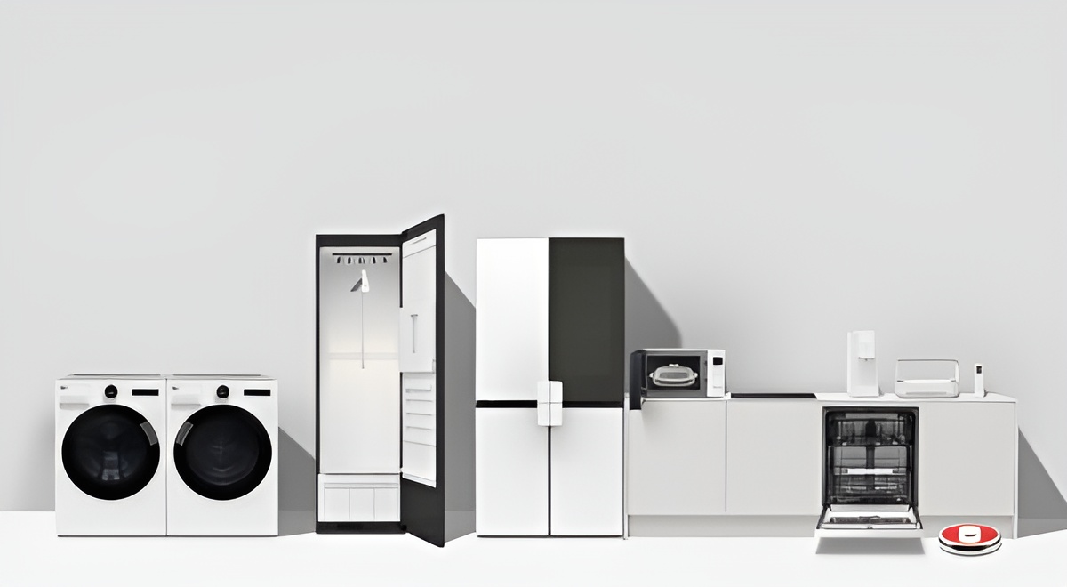 넓은 밝은 공간에 여러 생활가전이 일렬로 배치되어 있다. 왼쪽부터 흰색 전면 도어 세탁기와 건조기가 나란히 서 있고, 다음으로 문이 열린 의류관리기 내부가 보인다. 그 오른쪽에는 양문형 냉장고가 있고, 이어서 상부에 전자레인지와 정수기 형태의 작은 가전들이 놓인 하부장과 식기세척기가 설치되어 있다. 맨 오른쪽 바닥에는 원형 로봇청소기가 위치해 있다.