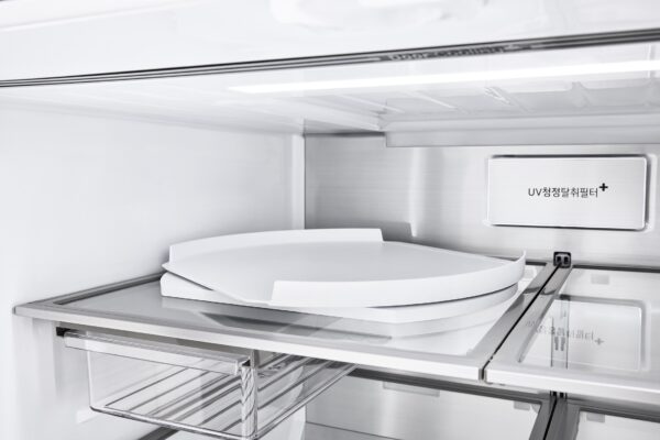 냉장고 내부를 비춘 사진으로, 투명 선반 위에 원형 회전 트레이가 놓여 있고, 내부 상단에는 밝은 조명이 켜져 있으며 ‘UV 청정 살균 필터+’ 표기가 보인다.