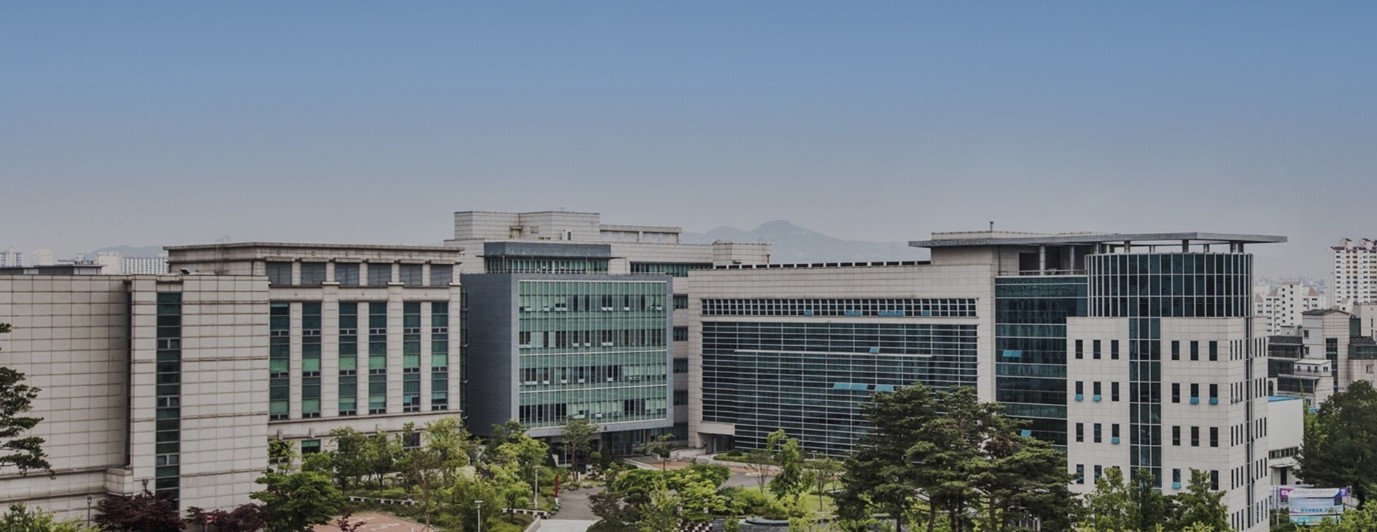 맑은 하늘 아래 촬영된 고려대학교 캠퍼스 전경 사진. 여러 동의 현대적인 회색·유리 외관 건물이 나란히 서 있고, 앞쪽에는 나무와 녹지가 보인다. 대학 건물들이 넓게 펼쳐진 전경을 담은 이미지다.